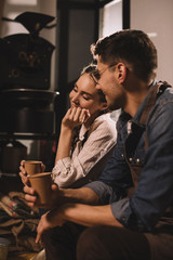 smiling couple with cups of coffee having break during work at coffee shop