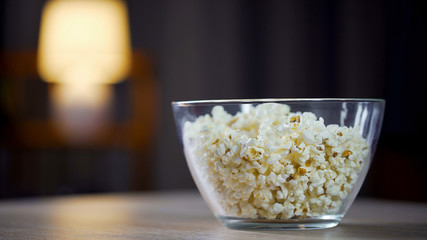 Big glass bowl of salty popcorn standing on table, treatment for home party