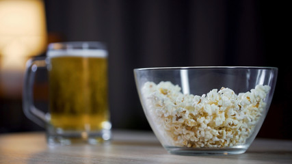 Glass bowl of popcorn and beer standing on table at home, lazy night at home