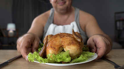 Smiling obese male looking at fatty grilled chicken, overeating and junk food