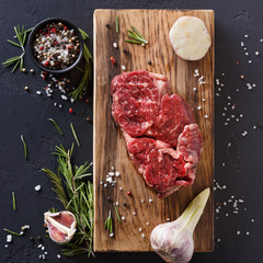 Rib eye steak and spices on wood at black background