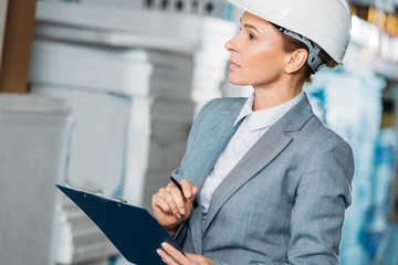 female inspector in helmet writing notes on clipboard in warehouse