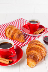 Freshly baked croissant on napkin, cup of coffee in red cup on white wooden background. French breakfast. Fresh pastries for breakfast. Delicious dessert. Closeup photography. Vertical banner