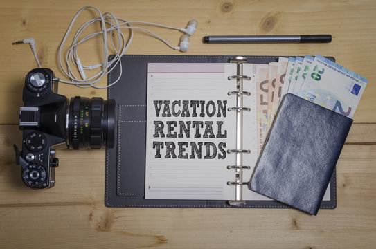 Vacation rental trends concept with notebook, photo camera, money and passport on wooden table background.