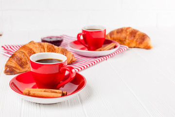 Freshly baked croissant on napkin, cup of coffee in red cup on white wooden background. French breakfast. Fresh pastries for breakfast. Delicious dessert. Closeup photography. Horizontal banner