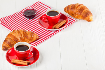 Freshly baked croissant on napkin, cup of coffee in red cup on white wooden background. French breakfast. Fresh pastries for breakfast. Delicious dessert. Closeup photography. Horizontal banner