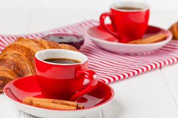 Freshly baked croissant on napkin, cup of coffee in red cup on white wooden background. French breakfast. Fresh pastries for breakfast. Delicious dessert. Closeup photography. Horizontal banner