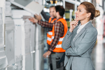 thoughtful inspector looking at shelves while men working behind in storehouse