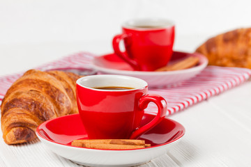 Freshly baked croissant on napkin, cup of coffee in red cup on white wooden background. French breakfast. Fresh pastries for breakfast. Delicious dessert. Closeup photography. Horizontal banner