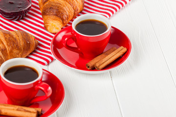 Freshly baked croissant on napkin, cup of coffee in red cup on white wooden background. French breakfast. Fresh pastries for breakfast. Delicious dessert. Closeup photography. Horizontal banner
