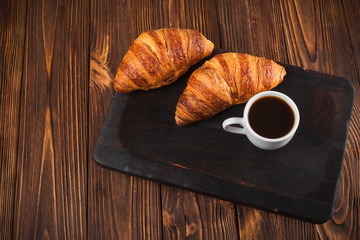 Freshly baked croissant jam, cup of coffee in white cup on brown wooden background. French breakfast. Fresh pastries for breakfast. Modern dark mood style. Delicious dessert. Horizontal banner