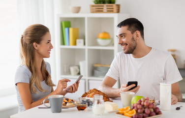 Obraz na płótnie Canvas couple with smartphones having breakfast at home