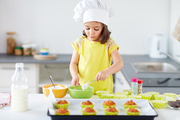 little girl in chefs toque baking muffins at home