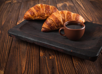 Freshly baked croissant jam, cup of coffee in white cup on brown wooden background. French breakfast. Fresh pastries for breakfast. Modern dark mood style. Delicious dessert. Horizontal banner