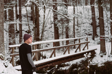 Fototapeta premium Young man running over a bridge in a forrest in Austria in the winter
