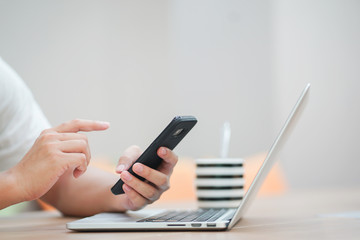 close up man hand holding smartphone and working with laptop at office room , business and technology concept