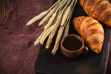 Freshly baked croissant jam, cup of coffee in white cup on brown wooden background. French breakfast. Fresh pastries for breakfast. Modern dark mood style. Delicious dessert. Horizontal banner