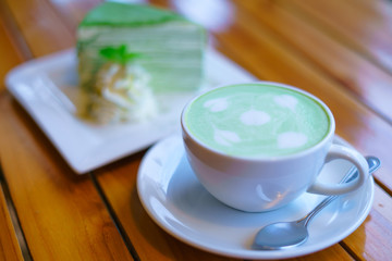 Selective focus.Hot matcha green tea latte with milk foam in a white cup and plate on old wooden table.