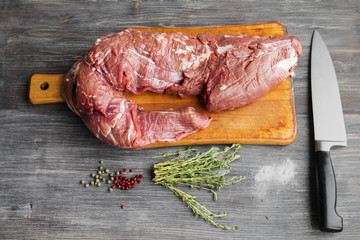 Raw red beef tenderloin on wooden kitchen board with green and pink pepper and thyme. Selective focus.