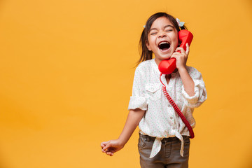 Screaming excited little girl child talking by red retro telephone.