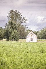 Green field, dramatic grey sky and old abandoned wooden barn and small house, Lonjsko Polje, Croatia