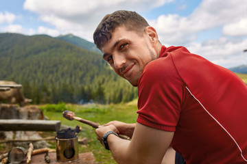 man in mountains cook on campfire in countryside
