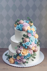 Beautiful three-tiered white wedding cake decorated with colorful flowers roses. Concept of elegant holiday desserts
