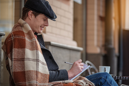 Side view of charming male with blanket relaxing with notebook and tea. Copy space in right side