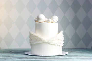 Rolgordijnen Feestelijke witte cake versierd met vleugels van mastiek en chocoladeballen erop. Concept ideeën desserts voor kinderen © Artem