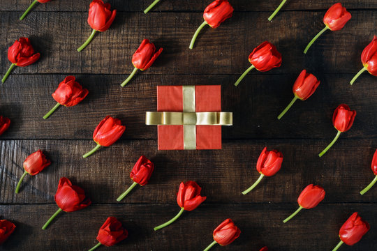 Red gift box with red tulips on dark wooden background