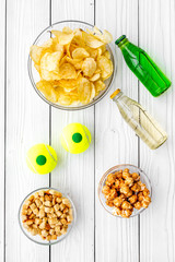Snacks for watching sport matches and games on TV. Crisps, popcorn, rusks near drink and ball on white wooden background top view