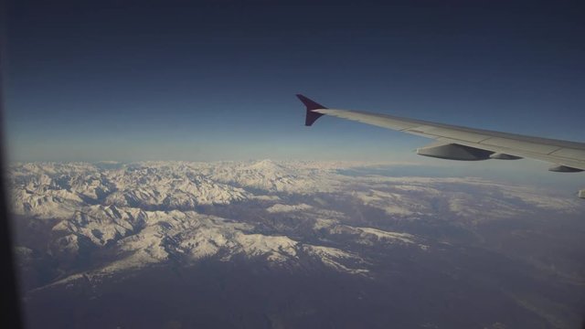 Mountain range with snow from the airplane window. Airplane wing. Aerial view on snowy mountains through window of an aircraft. Travel concept.