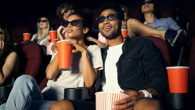 Young african man kissing his girlfriend whilesitting in cinema in 3d glasses and watching film