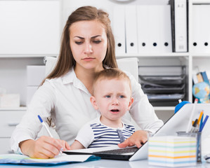 Serious girl with child is сoncentratedly working behind laptop