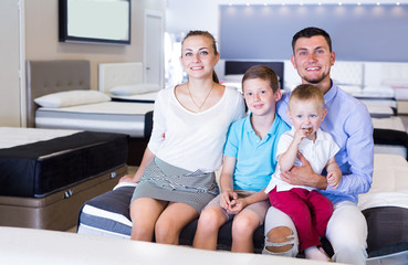 Obraz premium Young cheerful family sitting on bed in store