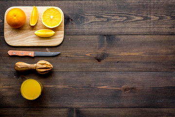 Healthy vitamin drink. Fresh orange juice near fruits and juicer on dark wooden background top view copyspace
