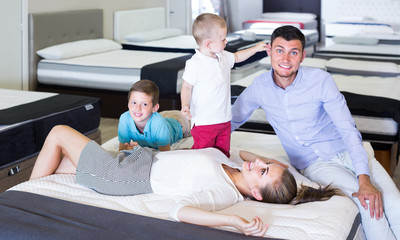 Young smiling woman with husband and sons lying on back on tested mattress in store