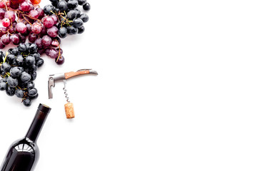 Fototapeta premium Uncorking the wine bottle. Bottle, corkscrew and bunches of red and black grapes on white background top view copyspace