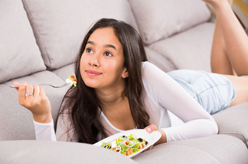 Obraz na płótnie Canvas Young smiling girl eating tasty salad