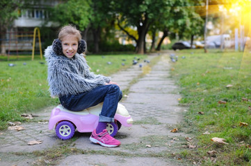 Teen girl rides on her youngest sister's pink car toys on street. She has a funny mood