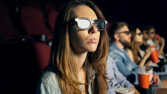 Young angry serious lady sitting in cinema and showing silence gesture while watching film