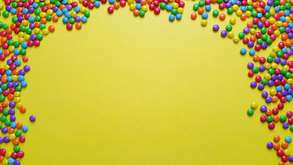 Frame of colorful confetti candy on yellow background
