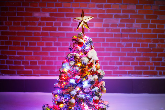 Christmas tree with festive lights in snow outdoors, purple brick wall background