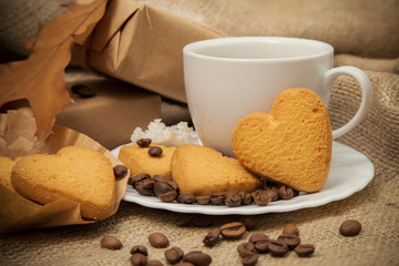  still life with a cup of coffee with milk, a cookie in the form of a heart, a gift on the background of coarse cloth
