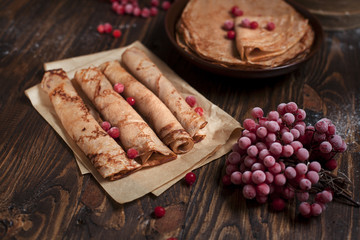 sweet fresh pancakes with a pile and pancakes on baking paper, rolled with tubules, viburnum berries on a dark wooden table on a dark gray background