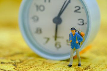 Travel and Time Concept. Traveller miniature figure with backpack walking on map with vintage round clock as backgroubnd