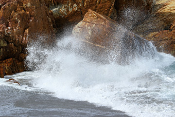 A big wave crashing into the rocks in the rough wild water of the ocean on a stormy during wintertime in South Africa.