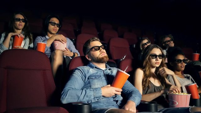 Tired bored multiethnic spectators in 3d glasses watching film in cinema