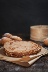 freshly baked sweet pancakes stacked on brown baking paper and croissants on a dark brown wooden table on a dark gray background