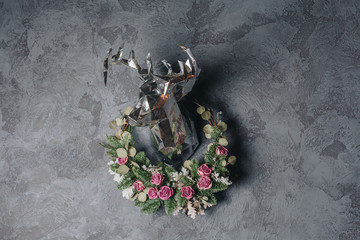 A silver polygon deer's head in the beautiful wreath of pink roses and pine branches on a grey background